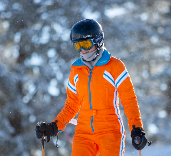 woman wearing tara shakti orange gloria one-piece snow suit skiing