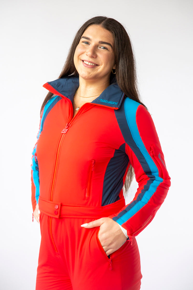 side closeup view model wearing tara shakti one-piece ski suit Diana variant red light and dark blue